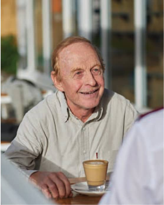 A older man smiles as he sips a warm coffee.